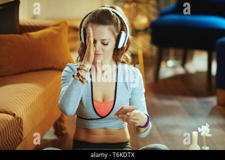 Giovane donna in sport vestiti nella casa moderna guardando lo yoga tutorial su internet tramite smartphone. Foto Stock