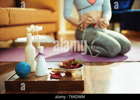 Primo piano sul vassoio con roba fragrante aroma per lo yoga e montare la donna scelta della musica per la meditazione in background in la casa moderna. Foto Stock