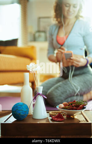 Primo piano sul vassoio con roba fragrante aroma per lo yoga e montare la donna scelta della musica per la meditazione in background in casa moderna. Foto Stock