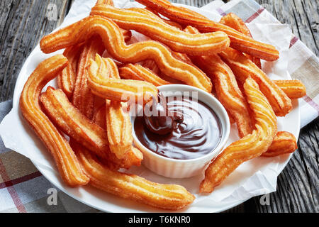 Deliziosi fritti churros servita con cioccolato immersione su una piastra bianca su una tavola di legno con tovagliolo, tradizionale spagnola e messicana street food Foto Stock