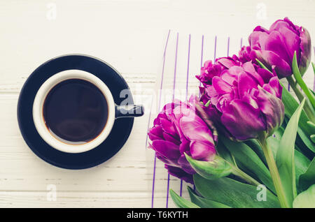 Tazza di caffè al mattino e bouquet di fiori di primavera tulipani bianco su sfondo di legno. Vista dall'alto. Mattina biglietto di auguri. Holiday, romanticismo della moderna l Foto Stock