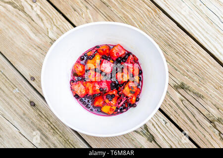 Appartamento vista dall'alto del rosso frutto di mango mirtilli vegetariano vegano insalata sul tavolo di legno nella ciotola e orange colori vibranti Foto Stock