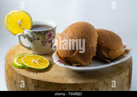 Due tipi di pane marrone su di una piastra e di una tazza calda di tè al limone sono collocati su un tappeto di legno con un isolato di sfondo bianco Foto Stock