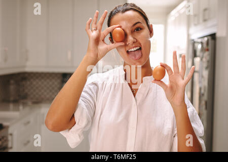 Funny donna marrone con uova fuori la sua linguetta in cucina. Pastry chef divertendosi in cucina. Foto Stock