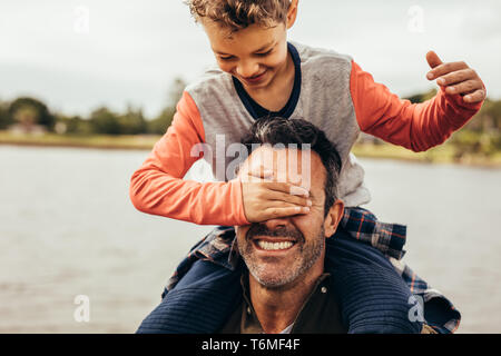 Padre e figlio il divertimento di trascorrere del tempo insieme a giocare all'aperto. Ragazzo chiudendo gli occhi di suo padre seduto sulle sue spalle. Foto Stock