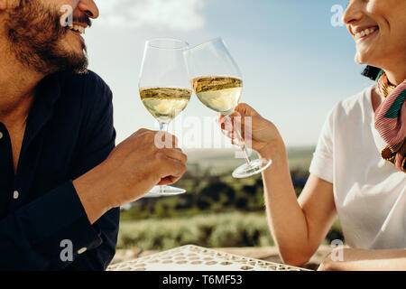 Tagliate il colpo di un giovane seduto insieme con i bicchieri di vino bianco in un vino data. Vista laterale di un giovane su una data di parlarsi tostare gl Foto Stock