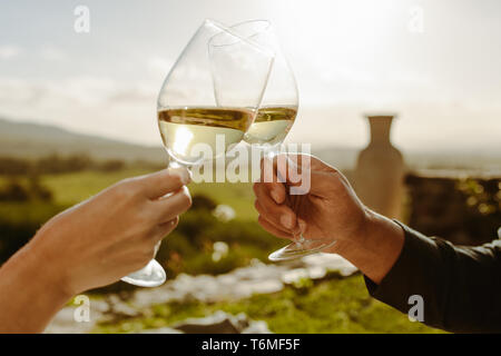 Chiudere fino alle mani di un paio di occhiali di tostatura di vino bianco. Tagliate il colpo di un paio di tostatura seduta del vino in un azienda vinicola. Foto Stock