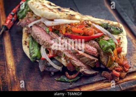 Barbecue invecchiato secco fianco wagyu steak chili assaporare e vegetale in un flatbread su una scheda di bruciato Foto Stock