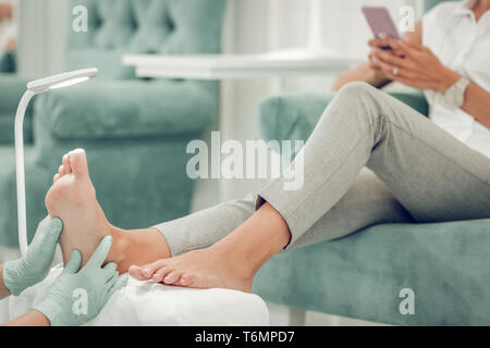 La donna in grigio pant comodamente seduto in poltrona di velluto Foto Stock