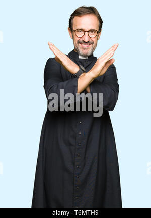 La mezza età sacerdote uomo indossare accappatoio cattolica rifiuto espressione bracci di incrocio facendo segno negativo, volto arrabbiato Foto Stock