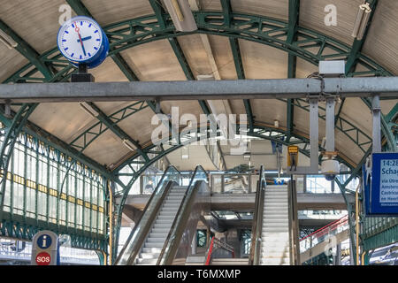 Stazione ferroviaria concourse con scale mobili, pannello informazioni e orologio Foto Stock