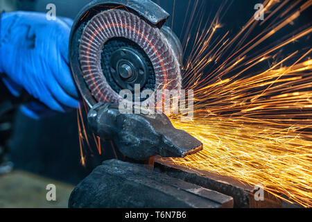 Saldatore professionale lavoratore in uniforme di protezione taglio tubo di metallo sul tavolo di lavoro con un macinino elettrico in officina industriale. Foto Stock