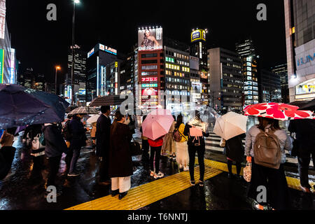 Shinjuku, Giappone - Aprile 1, 2019: Persone con ombrelloni in attesa crosswalk incrocio nel centro città con neon luminoso luci di notte durante la pioggia Foto Stock