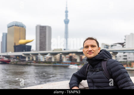 Tokyo, Giappone Sumida area distrettuale cityscape skyline con giovani turisti uomo appoggiato sulla ringhiera del ponte sul fiume nel centro cittadino sul giorno nuvoloso Foto Stock