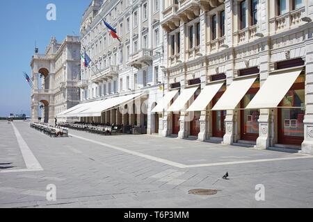 La facciata della casa con tende da sole e le righe vuote di sedie davanti a un caffè sulla Piazza Unita d' Italia, Trieste, Italia Foto Stock