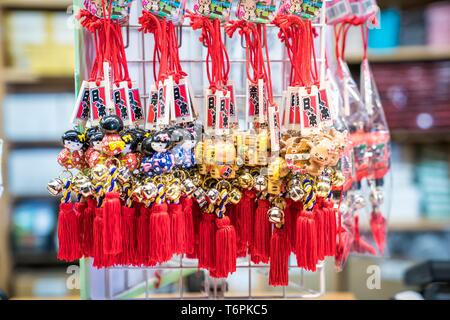 Prefettura di Nara, Giappone - 2 Mar 2018: giapponese amuleto con campana; ragazza in blu e rosso yukata, oro cat, cervi appendere al grill bianco per le vendite alle turiste Foto Stock
