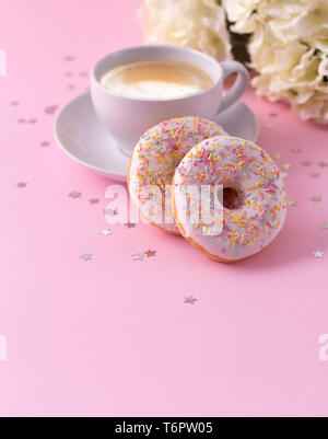 La tazza di cappuccino caldo e due ciambelle con Fiori su fondo rosa. Foto Stock