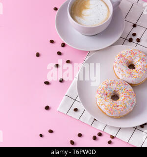 La tazza di cappuccino caldo con due ciambelle su un sfondo rosa Foto Stock