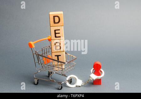 Blocchi di legno con la parola debito di un carrello per supermercati e una figurina umana legati da manette. Obbligo di pagamento del debito. Alimenti il pagamento. Pagare Foto Stock