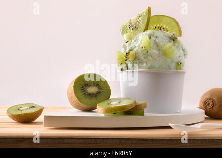 Kiwi coppa di gelato decorata con pezzi e fette di kiwi su un tavolo di legno. Composizione orizzontale. Vista frontale. Foto Stock