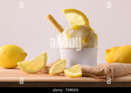 Coppa di gelato al limone decorata con spicchi di limone su un tavolo di legno. Composizione orizzontale. Vista frontale. Foto Stock