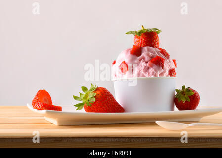 Bicchiere di gelato alla fragola decorata con pezzi di frutta su una piastra su un tavolo di legno. Composizione orizzontale. Vista frontale. Foto Stock