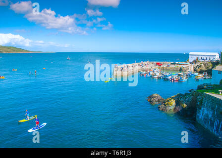 Porto Coverack in Corwall, su una intensa giornata di sole. Paddle boarders sono in acqua e quindi non vi è molto acrivity sulla parete del porto. Foto Stock