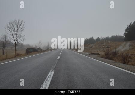 Dritto su strada di montagna scomparendo a distanza su un nebbioso giorno Foto Stock