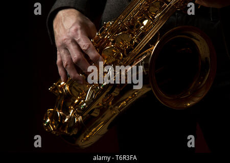 Primo piano del sassofono tenore suonato dal musicista caucasico maschile, la sua mano destra in posizione sullo strumento. Sassofonista isolato. Foto Stock