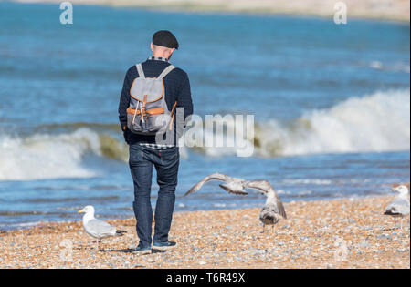 Uomo che cammina da sola portando uno zaino su una spiaggia in primavera nel Regno Unito. Foto Stock