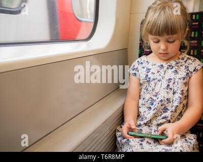 Ragazza carina durante la riproduzione su telefono cellulare su un treno Foto Stock