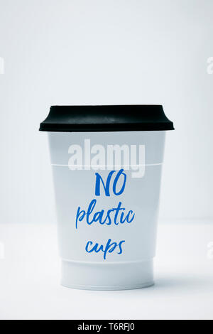 Primo piano di un bianco tazza di plastica con il testo non bicchieri di plastica scritto in esso, coperto con un coperchio nero su sfondo bianco Foto Stock