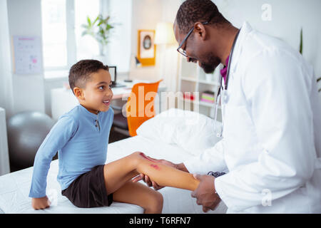 Carino piccolo ragazzo visita pediatra dopo graffiare la sua gamba Foto Stock