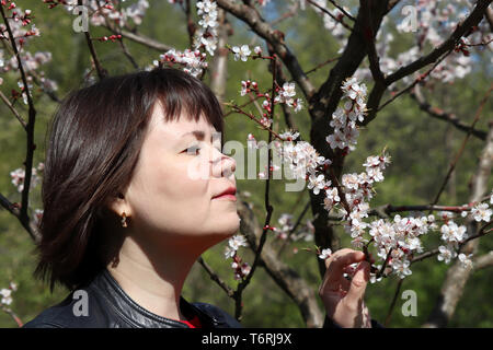 Felice giovane donna profumati fiori di sakura. La fioritura dei ciliegi nel giardino primaverile, romantico ritratto Foto Stock