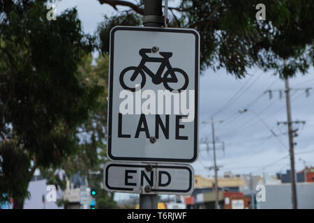 Bike lane end firmare con sovrastante i rami degli alberi, cielo nuvoloso e linee di alimentazione in background in Melbourne, Australia Foto Stock