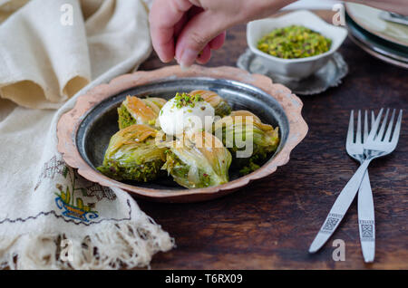 Dolce turco Baklava con gelato sulla piastra di rame. La donna è mettere i pistacchi su la baklava. Foto Stock