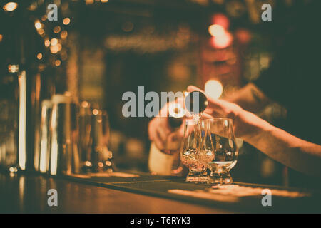 Immagine ravvicinata di un barman versando il whisky in un bicchiere Glencairn. Foto Stock