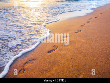 Spiaggia, onde e impronte in tempo al tramonto Foto Stock