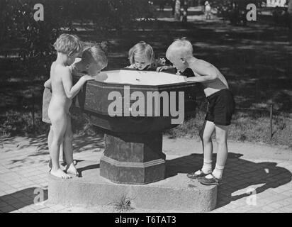 Estate di 1940s. Quattro bambini sono acqua potabile da una fontana di acqua in uno dei parchi di Stoccolma. Queste fontane pubbliche erano comuni e in questo momento è azionato spingendo la leva verso il basso e che l'acqua ha iniziato a flusso. La Svezia 1940s Foto Stock