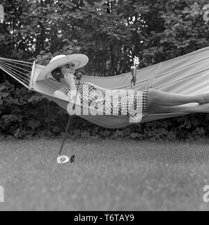 Estate negli anni sessanta. Una signora è comodamente sdraiato in una amaca parlando al telefono. La Svezia 1961 Foto Stock