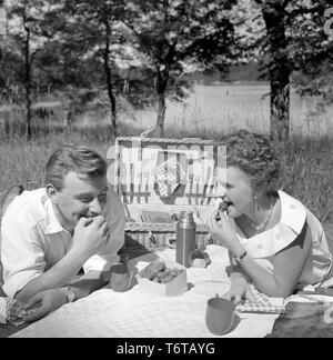 Picnic negli anni cinquanta. Una giovane coppia stanno godendo una giornata di sole. Essi hanno gremito il loro cibo e bevande nella pratica custodia per picnic. Essi sono di mangiare fragole fresche. La Svezia 1956 Foto Stock