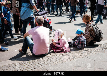 Berlino, Germania - 01 May 2019: giovane famiglia con bambini seduti sul marciapiede sulla street parade il giorno della festa del lavoro a Berlino Foto Stock