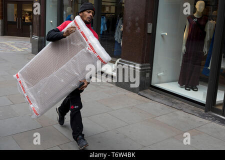 Un corriere con dpd trasporta un pacchetto avvolto in Bubble Wrap lungo Long Acre vicino a Covent Garden, il 2 maggio 2019, a Londra, in Inghilterra. Foto Stock