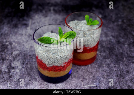 Chia il grano con il latte dolce con lampone e fragola berry il riempimento in bicchieri di vetro con foglia di menta Foto Stock