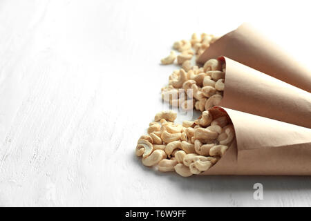 Coni di carta con gustosi noci di acagiù bianco su sfondo di legno Foto Stock