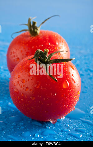 Due rossi pomodori ciliegia su uno sfondo blu Foto Stock
