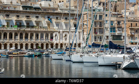 Barche a motore bianche e imbarcazioni da diporto nel Grand Harbour Marina di Vittoriosa, con gli storici edifici calcarei di Senglea che costeggiano il lungomare Foto Stock