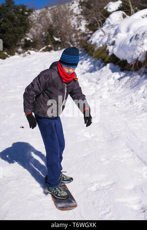 Vista frontale del ragazzo lo snowboard su skateboard in una coperta di neve hill Foto Stock