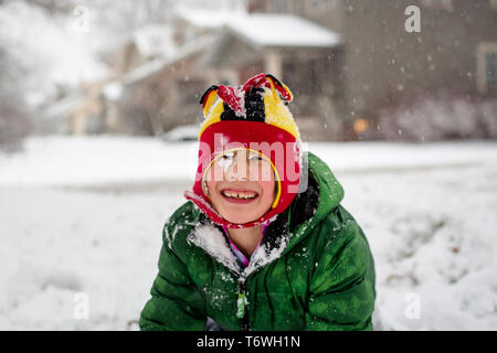 Un gioioso coperte di neve bambino in un fuzzy hat gioca in una tempesta di neve Foto Stock