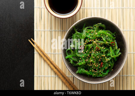Alghe Wakame insalata con semi di sesamo e peperoncino in una ciotola su una stuoia di bambù Foto Stock